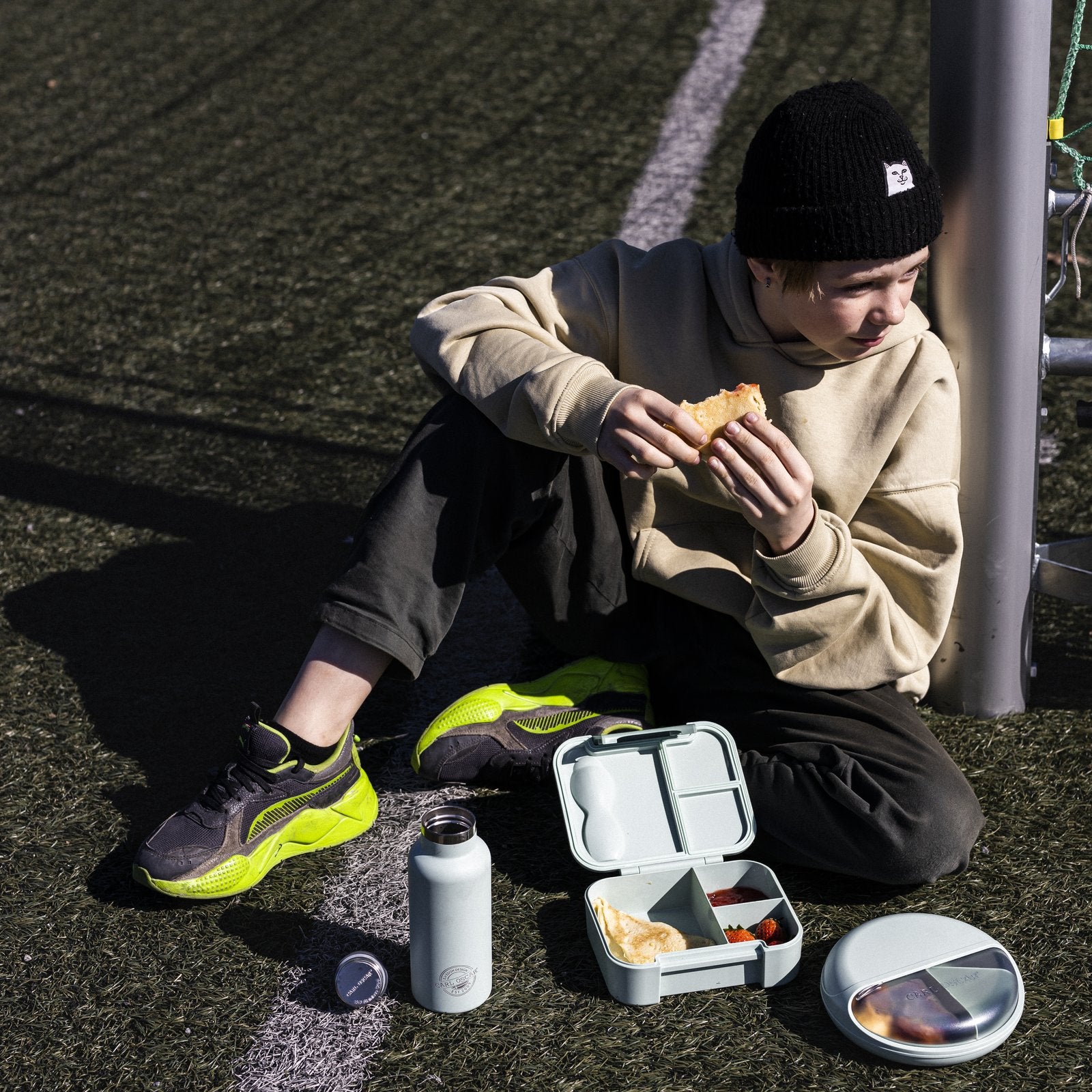 Niño en cancha con lonchera, termo y SnackDisc Carl Oscar — productos disponibles en Mamá Porqué Chile